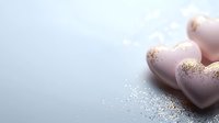 Pink heart-shaped chocolates with gold glitter dust scattered on light blue surface, romantic confectionery background for Valentine's Day and special occasions.