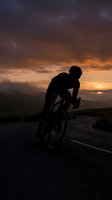 Silhouette of male cyclist in aerodynamic position riding road bike against dramatic sunset sky with orange and purple clouds on mountain highway.