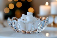 White sugar cubes in crystal glass bowl against soft bokeh lights and candles, creating elegant mood for tea service or dining table decoration.