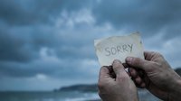 Hands holding sorry note against dramatic stormy sky background expressing apology regret forgiveness reconciliation emotional communication concept.