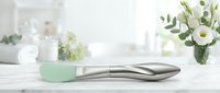Modern stainless steel kitchen utensil with mint green silicone handle on white marble countertop. Contemporary cookware for culinary preparation and cooking.