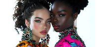Two diverse fashion models with curly hairstyles wearing colorful outfits and ornate statement jewelry against white background. Perfect for beauty and fashion campaigns.