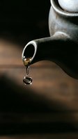 Close-up of a rustic ceramic teapot spout with a dripping tea drop reflecting the word TEA, captured in moody dark tones.