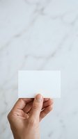 Cropped hand holding blank white card against marble background, isolated on clean surface for business card mockup, branding, and corporate identity design.