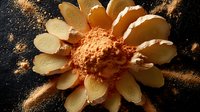Artistic arrangement of sliced yellow apple in sunflower shape with cinnamon powder sprinkled on dark background creating dramatic food photography composition.