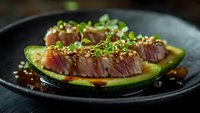 Seared tuna steak slices with sesame seeds and microgreens served on avocado halves in dark ceramic bowl for gourmet restaurant presentation.