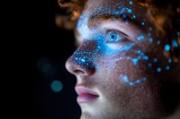 Young woman with freckles in profile view against dark background, glowing blue dots scattered across face creating magical ethereal effect for beauty and technology concepts.