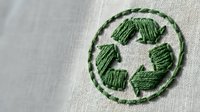 Green recycling symbol embroidered on natural fabric background for eco-friendly sustainable design projects and environmental awareness campaigns.