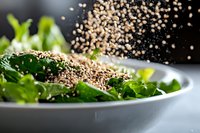 Fresh green salad with quinoa grains falling in motion, close-up view on white ceramic plate against dark background, healthy eating concept.