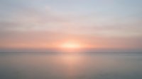 Serene sunrise over calm ocean waters with soft pink and golden light reflecting on the horizon, conveying tranquility and peaceful morning atmosphere for wellness and nature projects.
