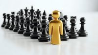 Golden figure standing out among black chess pieces representing leadership and strategic thinking in business competition.