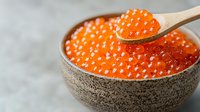 Fresh red caviar in ceramic bowl with wooden spoon. Bright orange salmon roe close up on gray background. Luxury seafood delicacy for gourmet appetizer.