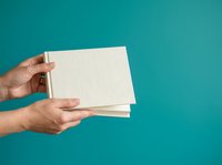 Hands holding blank white notepad against turquoise background for stationery, branding, and product mockup designs.