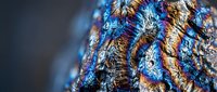 Iridescent bismuth crystal formation displaying rainbow metallic colors and geometric stepped structure against dark background for science education materials.