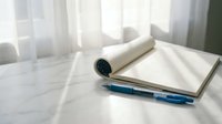 Rolled diploma certificate with blue ribbon on white table near window with natural light for graduation ceremony and academic achievement celebration.
