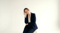 Stressed businesswoman in dark suit holding head in hand showing workplace burnout and mental fatigue on neutral background.