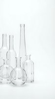 Empty clear glass bottles of various shapes and sizes arranged on white background for minimalist design and packaging concepts.
