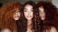 Three young women with different shades of curly hair posing together, showcasing natural beauty and diverse hair textures in warm tones.