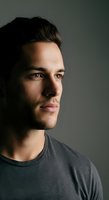 Young man with dark hair and facial stubble wearing casual gray t-shirt, looking thoughtfully to side against neutral background. Suitable for lifestyle, business, and portrait projects.