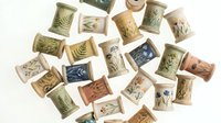 Handmade ceramic tiles with botanical leaf imprints in earthy tones scattered on white background, artisan pottery craft supplies for home decor projects.