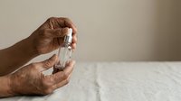 Mature man with medium skin tone holding clear glass perfume bottle with dropper applicator against neutral background for fragrance marketing.