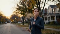 Middle-aged Caucasian woman jogging through a suburban neighborhood in autumn, wearing athletic wear, staying active and healthy outdoors.