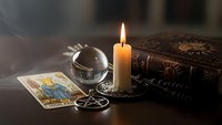 Mystical fortune telling setup with burning candle, crystal ball, tarot cards and ancient books on wooden table for divination and spiritual guidance.