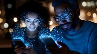 Young diverse couple looking at glowing smartphones with magical blue digital particle effect overlay at night, representing digital connectivity and social media.