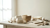 Rustic wooden kitchen utensils and ceramic bowls arranged on natural wood table in bright minimalist interior for cooking and food preparation.