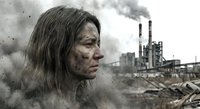 Exhausted woman with dirty face in polluted industrial wasteland with smoking factory chimneys and environmental destruction in background.