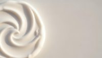 Creamy white swirl texture with smooth flowing curves creating elegant spiral pattern on neutral beige background for luxury cosmetic and skincare designs.
