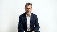 Middle-aged man with salt-and-pepper hair and facial hair wearing navy blazer over white shirt, seated against white background for corporate, business, and professional portrait use.