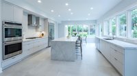 Modern white kitchen with marble island and stainless steel appliances in bright contemporary home interior with large windows and natural light.