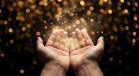 Open cupped hands releasing magical golden light particles and sparkles against warm bokeh background for spiritual and inspirational concepts.