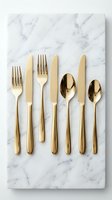 Elegant gold flatware set arranged on white marble surface, featuring forks, knives, and spoons with polished metallic handles for fine dining and upscale table settings.