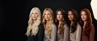 Five diverse women with different hair colors from blonde to brunette to red standing together in neutral clothing against dark background for beauty diversity concept.