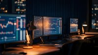 Financial analyst workspace with multiple monitors displaying stock market charts and trading data in modern office at night for investment analysis.
