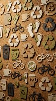 Eco-friendly cardboard cutout icons on cork board, featuring recycling symbols, bicycles, footprints, and coffee cups for sustainability concepts.