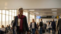 Happy young African American woman walking through busy airport terminal with luggage, smiling while traveling for business or vacation.