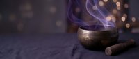 Tibetan singing bowl with incense smoke and warm bokeh lights creating peaceful meditation atmosphere for wellness and spiritual practices.