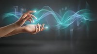 Human hands cupping glowing turquoise energy waves in dark space representing healing power, spiritual connection and electromagnetic fields for wellness concepts.