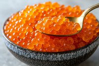 Fresh red caviar in black ceramic bowl with silver spoon, bright orange salmon roe pearls close up showing delicate texture and translucent shine.