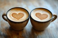 Two ceramic cups of latte with heart-shaped foam art on wooden surface, romantic coffee composition for cafe menu and valentine designs.