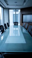 Modern corporate boardroom with glass conference table and black chairs in contemporary office building with city view for business meetings.