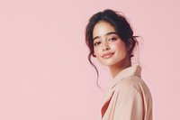 Young Asian woman with natural makeup and messy updo hairstyle wearing beige blazer smiling confidently against pink background. Professional portrait for beauty and fashion.