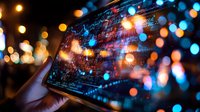 Digital tablet screen showing data analytics against blurred bokeh lights background, creating futuristic technology atmosphere with orange and blue glow.