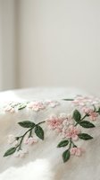 Delicate pink floral embroidery on natural linen fabric with green leaves, handcrafted needlework detail for home decor and textile design projects.