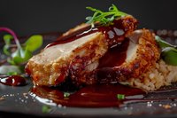 Sliced crispy chicken breast with sweet and savory teriyaki sauce drizzle over steamed rice, garnished with fresh microgreens on dark plate.
