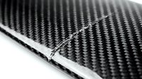 Black carbon fiber composite material with visible crack damage showing structural failure and material weakness for engineering analysis.