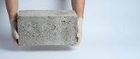 Male hands holding a rectangular concrete block or cinder brick against a white background, suitable for construction, building materials, and industrial concepts.